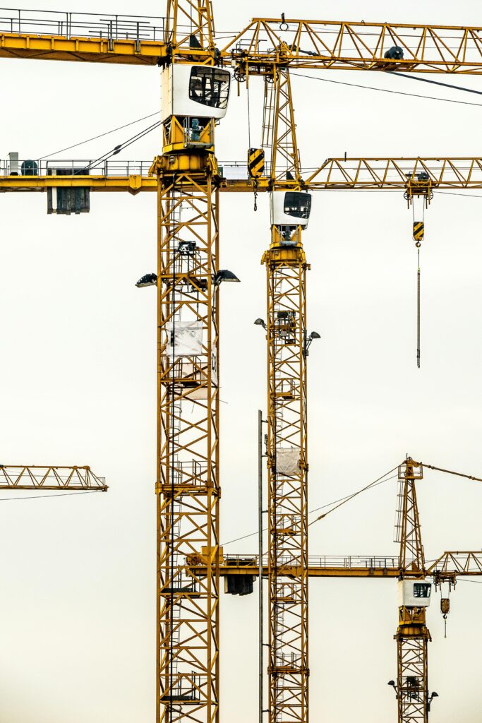 Vertical shot of multiple construction cranes towering against a cloudy sky.